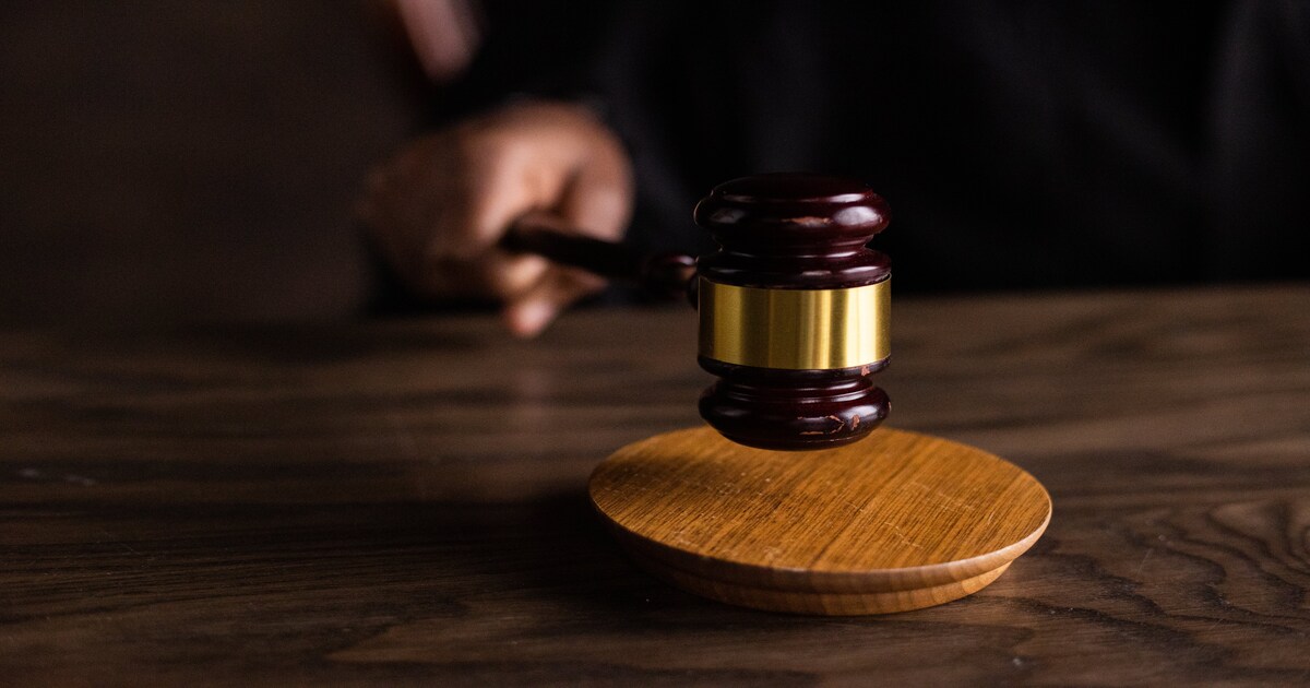 A person holding and using a gavel on a wooden table.